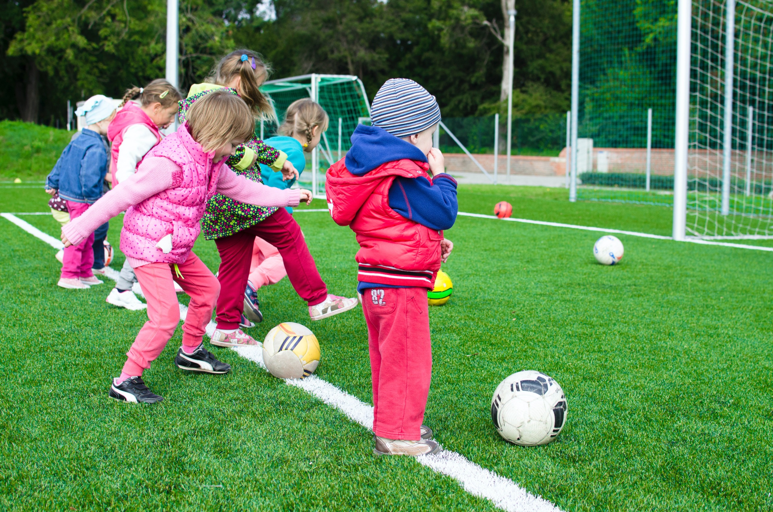 Children lined up at a goal line with soccer balls, waiting to kick the ball into the soccer net